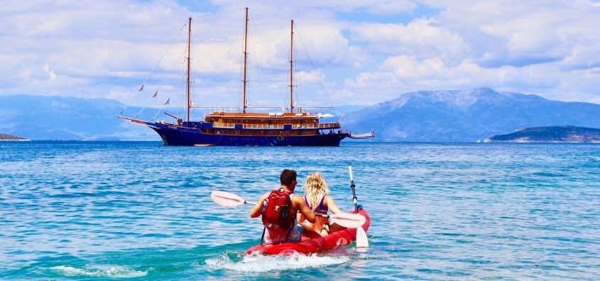 Couple kayaking near a traditional small cruise ship in Greece with crystal-clear waters