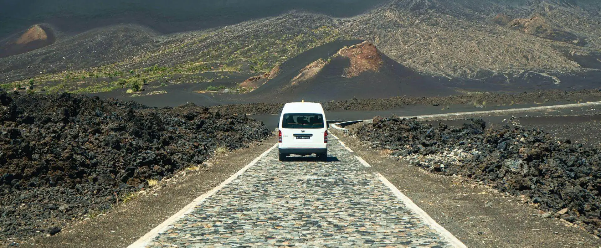 A Cape Verde cruise excursion through volcanic landscapes, featuring a van on a cobbled road.