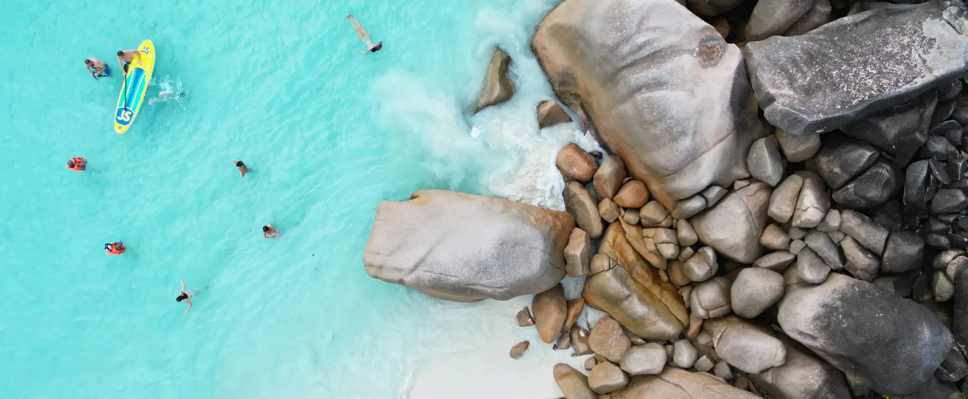 A group of travellers swimming and paddleboarding in clear turquoise waters near rocky shores, enjoying sustainable travel