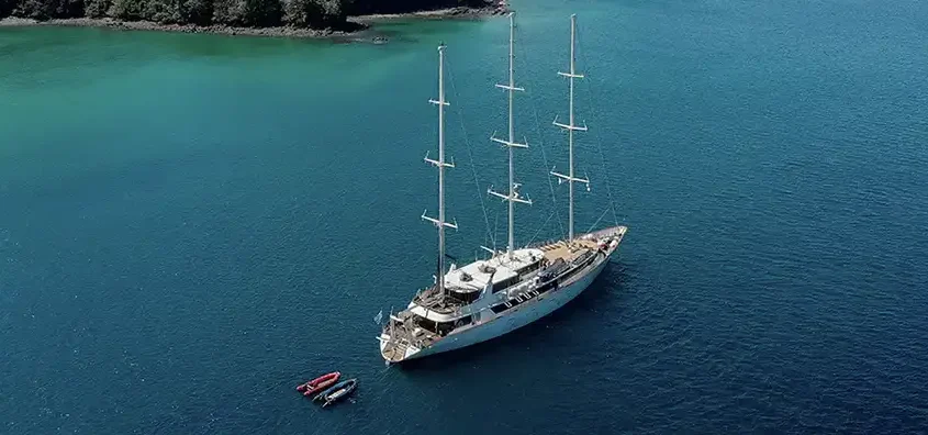 A traditional ship with white sails cruising along a scenic coastline, promoting sustainable travel