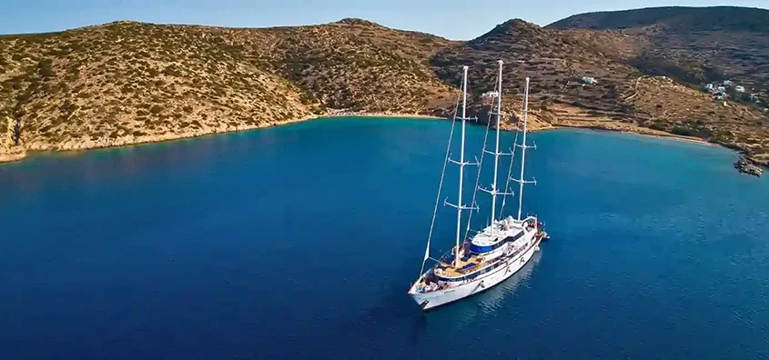A small ship cruise anchored in a secluded bay with crystal-clear waters and rugged hills