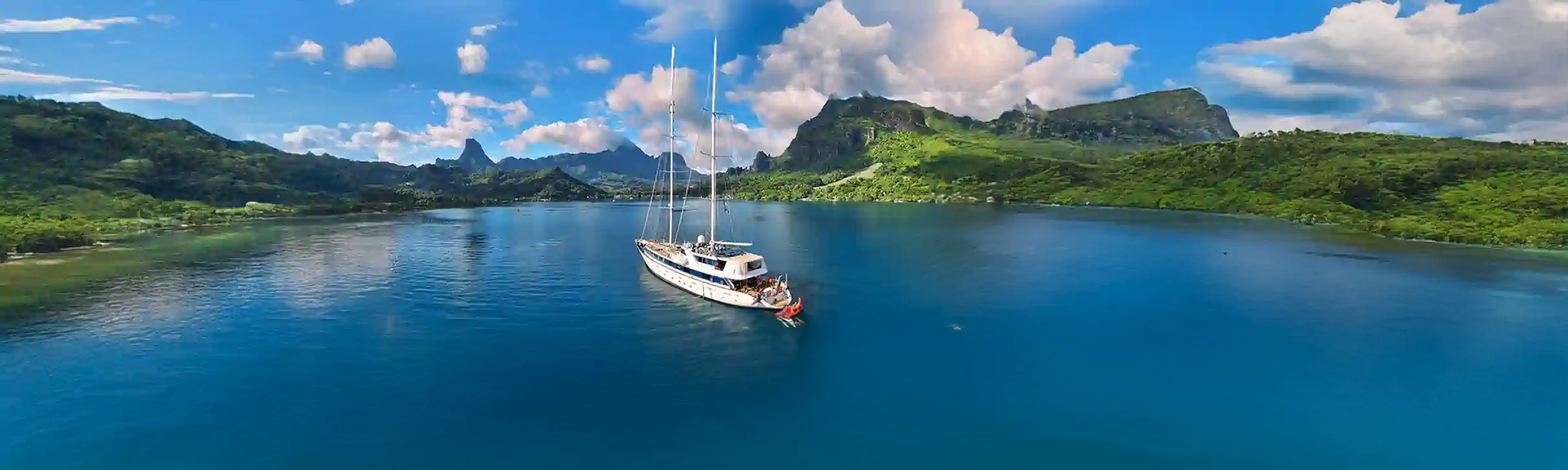 Small ship at anchor in a tranquil bay in French Polynesia, ringed by green mountains