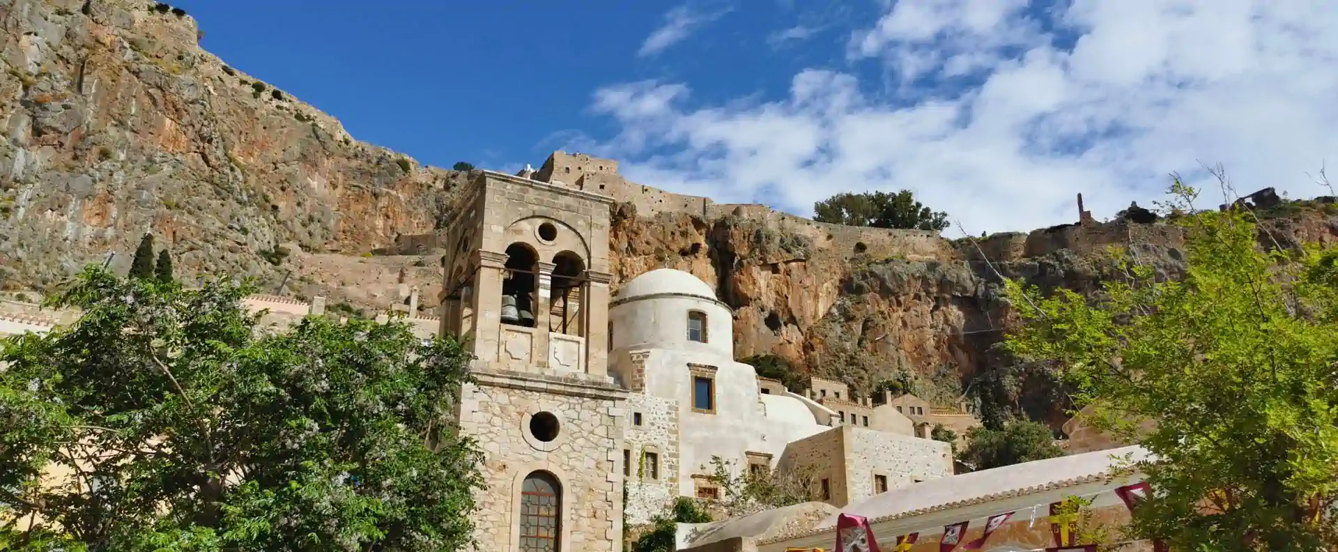 cyclades-cruise-itinerary-monemvasia-bell-tower.webp Bell tower and white-dome church against dramatic rock face—a cultural highlight along the Cyclades cruise itinerary.