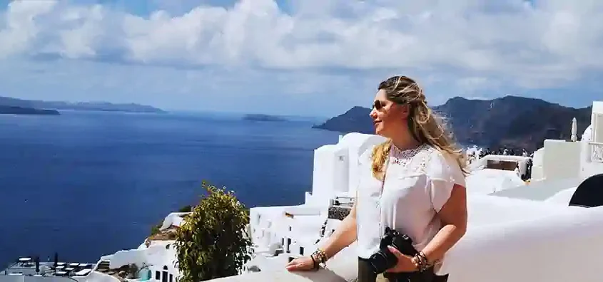 Traveller on a Cyclades cruise itinerary admiring the deep-blue Aegean from a clifftop terrace in Santorini, camera in hand.