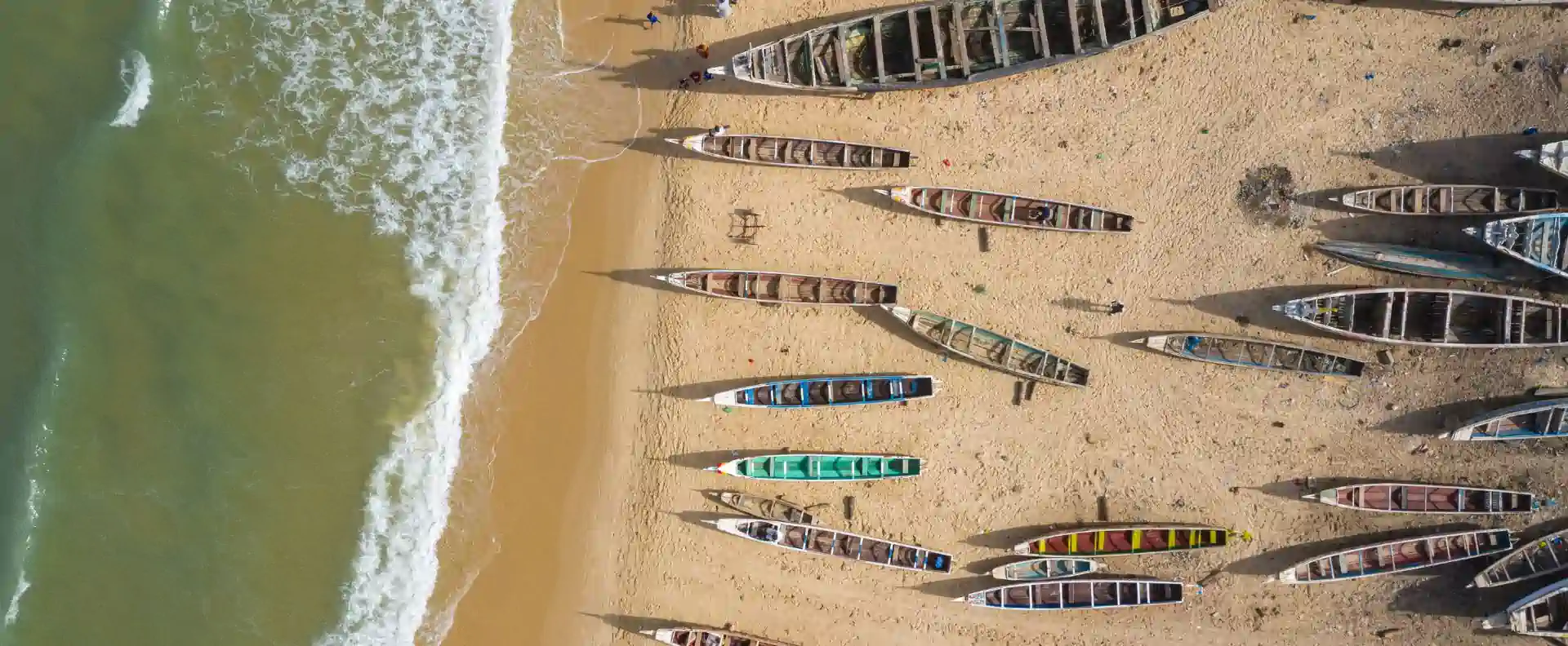 west africa cruises traditional pirogues beach Traditional West African fishing boats lined up on a sandy beach near the Gambia River, seen from above.