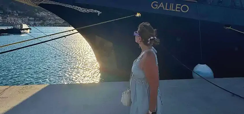 Nellie on the quay looking toward MS Galileo’s bow at sunset in Marina Zea during a Greek coastal cruise.