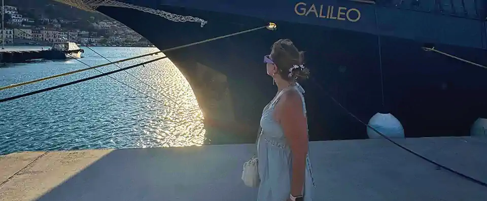 Nellie on the quay looking toward MS Galileo’s bow at sunset in Marina Zea during a Greek coastal cruise.
