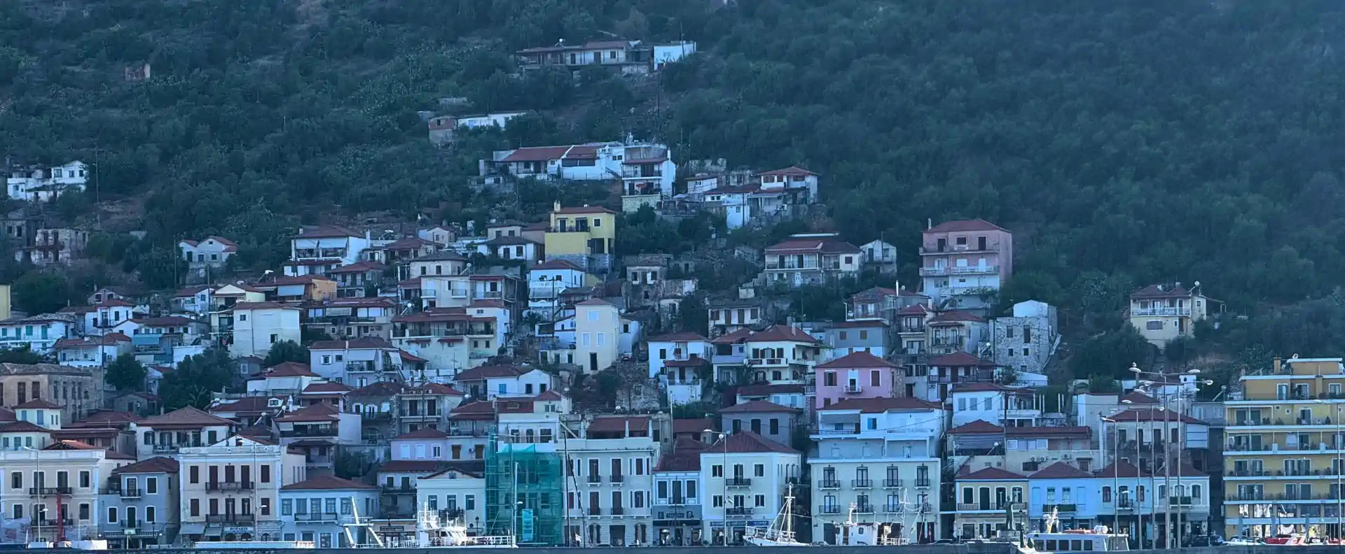 Hillside homes above a Peloponnese harbour town viewed from the water during a Greek coastal cruise.