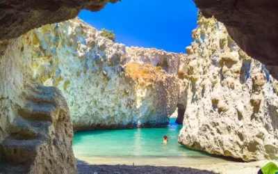 Greek island cruises to a turquoise cove framed by a rocky sea cave on Milos, Greece