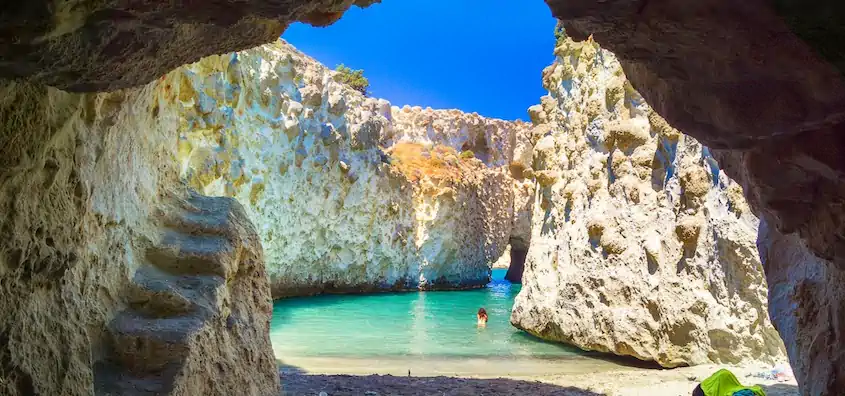 Greek island cruises to a turquoise cove framed by a rocky sea cave on Milos, Greece
