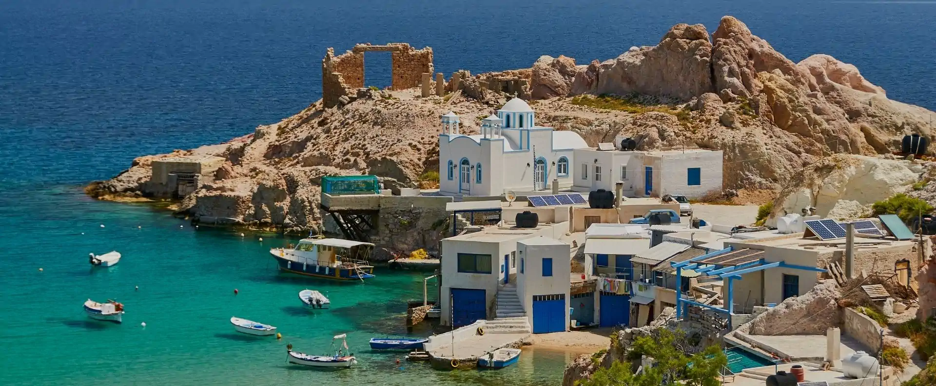 Greek island cruises to Klima fishing village in Milos, with whitewashed houses, small boats and turquoise water.