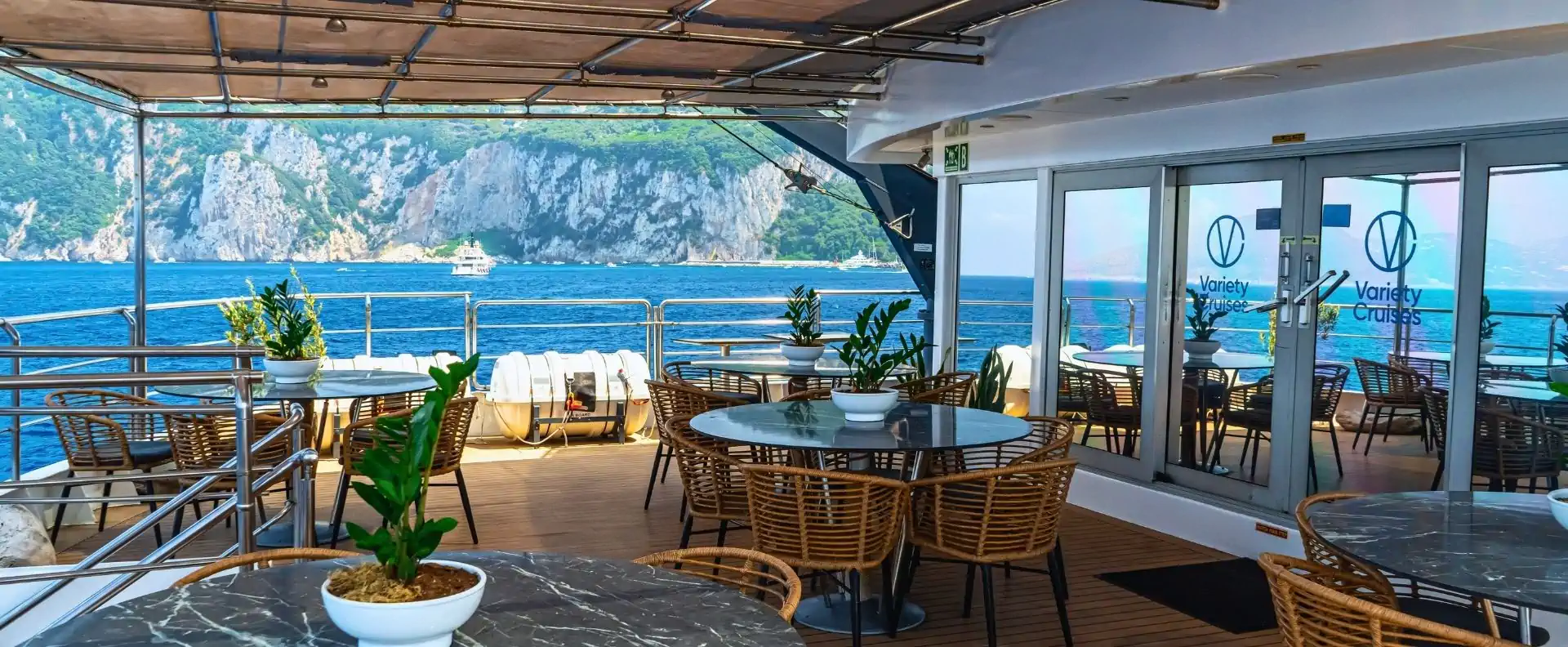 small ship shaded deck sea view Shaded outdoor deck with round tables and wicker chairs looking out over the sea and cliffs on a small ship cruise